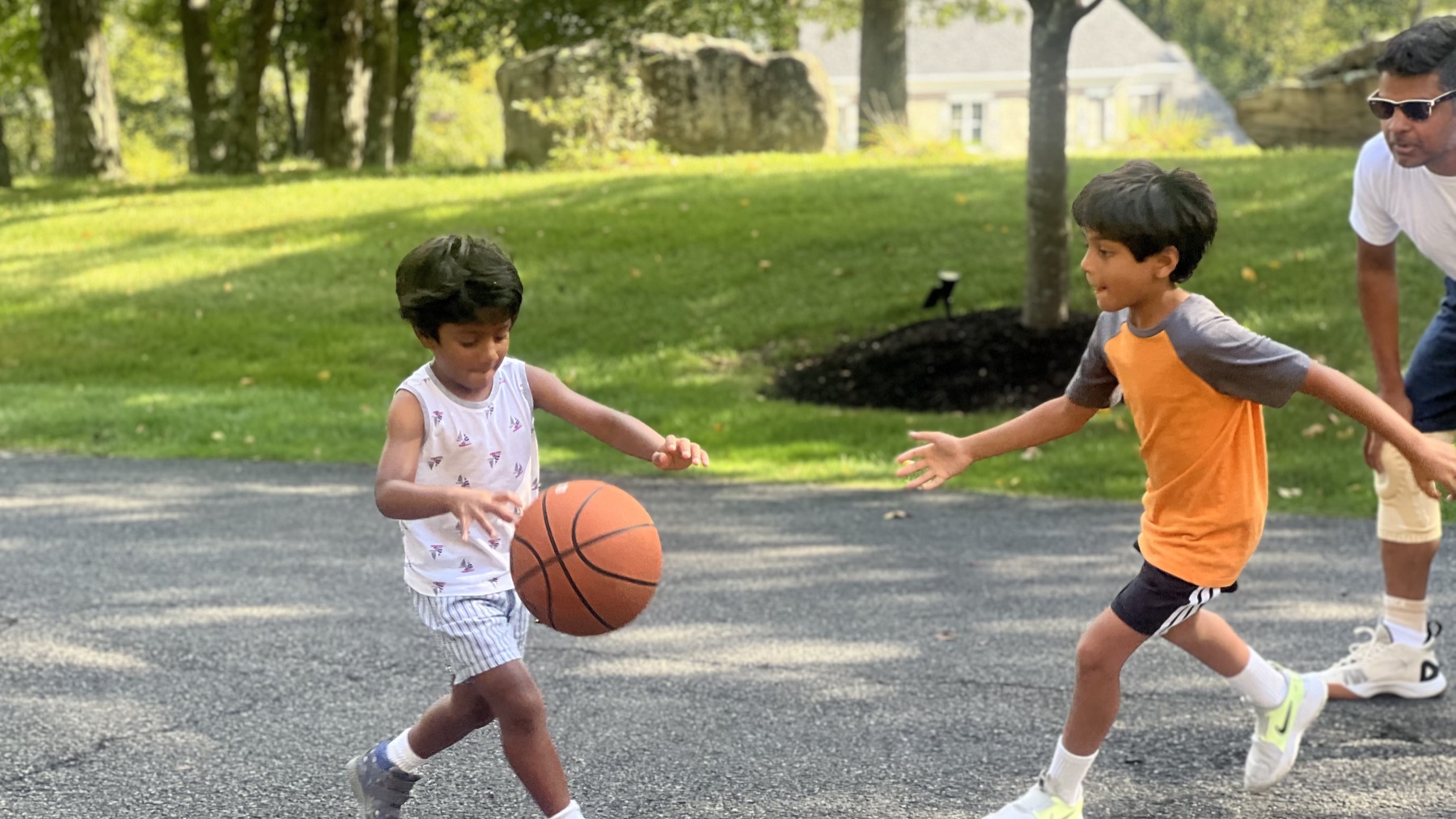 Aakash and Aarjun Etwaru playing basketball on the driveway while Richie Etwaru moves in to defend.